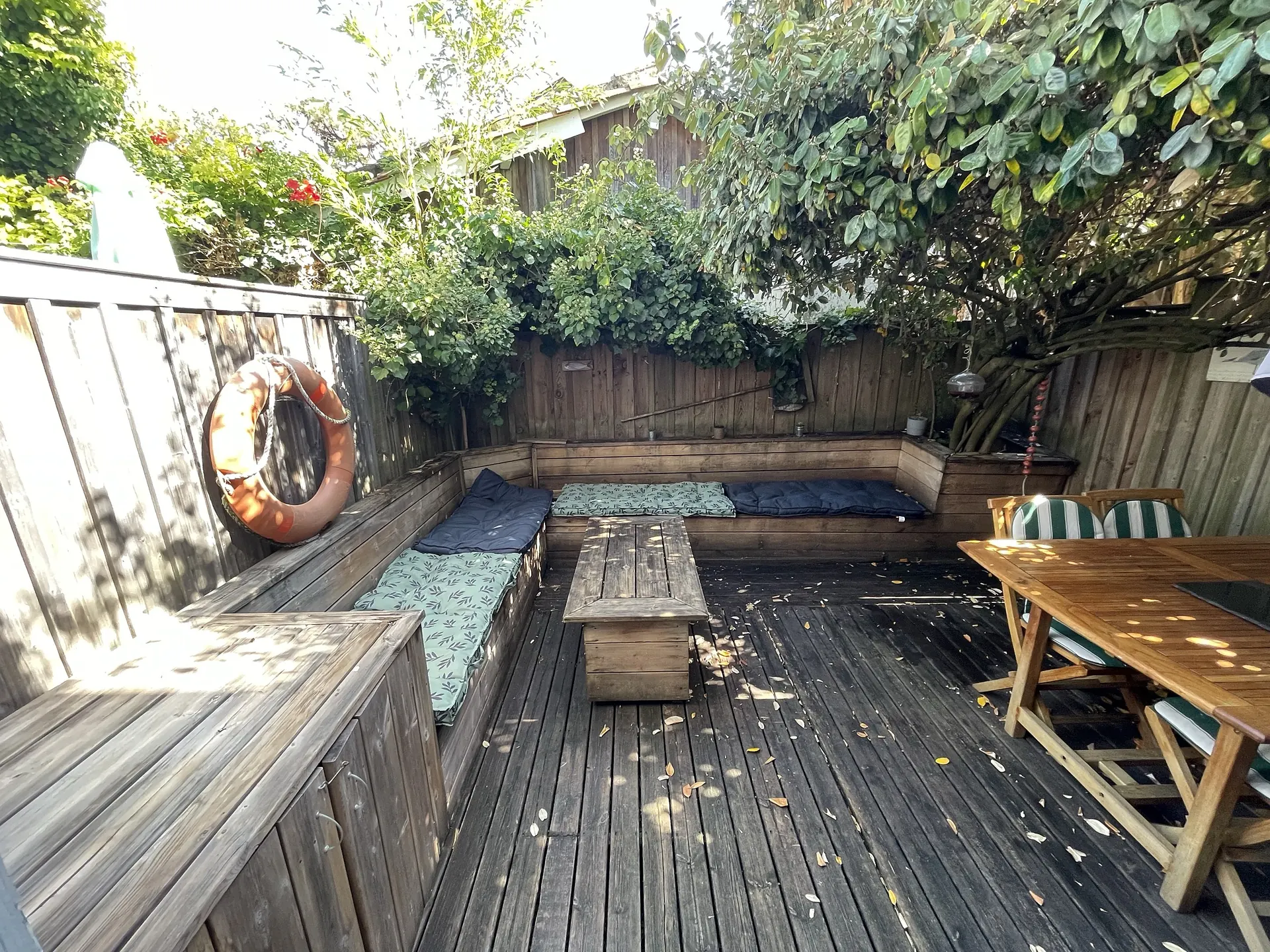 The terrace in full sun, enclosed by its wooden fence and greenery